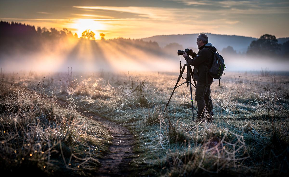 Illustration von einem Naturfotografen, der in der Morgensonne das goldene Streiflicht für Landschaftsaufnahmen nutzt